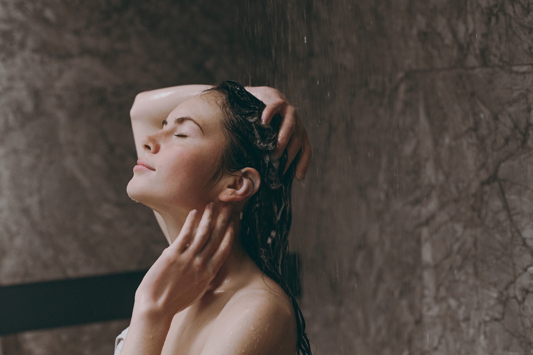 A woman rinsing her hair in a warm stone shower